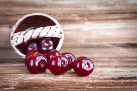 Cherry berries spilled out of a decorative basket on a wooden background. Copy spaceの写真素材