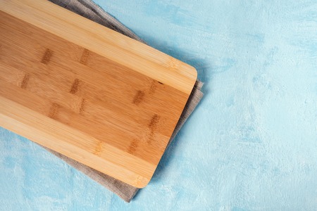 Wooden cutting Board and linen towel on blue background.