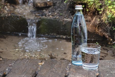 Glass bottle and glass with water on the background of nature. Spring water