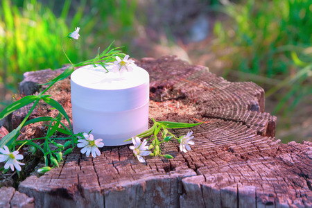 White jar with cosmetic cream on a wooden stump with wildflowers and green grass on a bright summer Sunny dayの写真素材