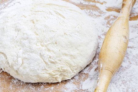 Rolling pin, dough and flour on a wooden board close-up