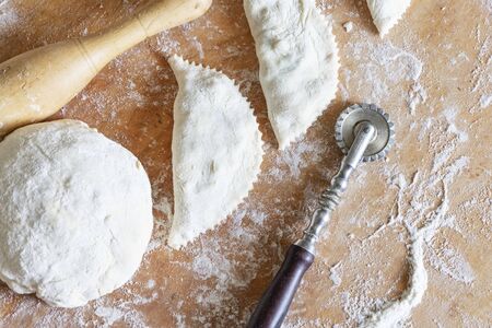 Cooking patty. The dough, rolling pin and raw pies on the table.