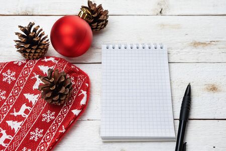 Christmas background. Stocking, cones, red ball, Notepad and pen on white wooden background. Paper for notesの写真素材