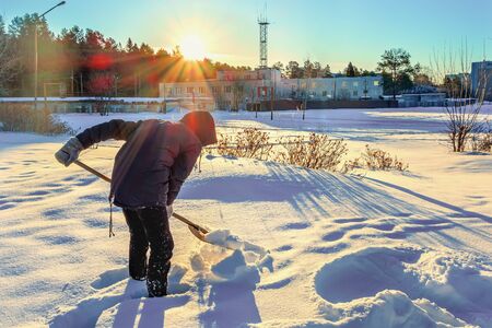 Teenager cleans the road from the snow with a wooden shovel. Sunny frosty winter dayの写真素材