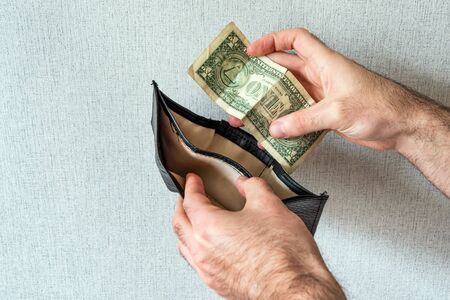 Men's hands hold one dollar and an empty wallet. The concept of bankruptcy, debt, financial problems