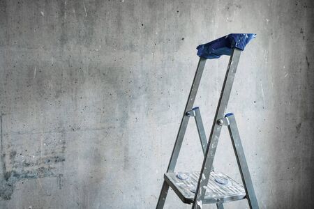 A step ladder smeared with white paint against a gray concrete wall for room repairsの写真素材