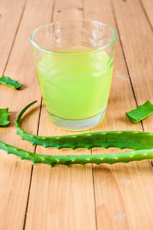 Aloe Vera juice in a glass and fresh aloe leaves on a wooden background. Vertical imageの写真素材