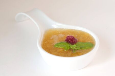 Sweet peach sauce in white spoon decorated with raspberry and mintの写真素材