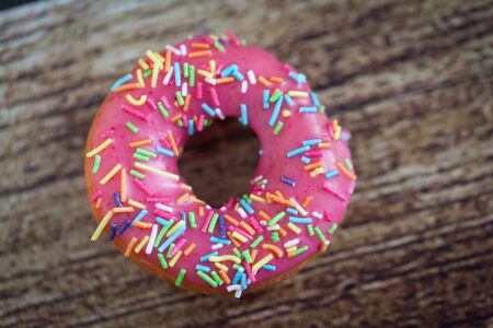Donut with pink icing and color sprinkles on wooden backgroundの写真素材