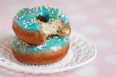 Donuts with blue icing and color sprinkles in knitted saucer on pink backgroundの写真素材