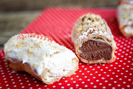 Chocolate and icing topping eclairs with chocolate and vanilla cream stuffing  on red fabric with...