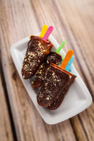 Vanilla ice-cream lolly covered with chocolate and almonds on color sticksの写真素材