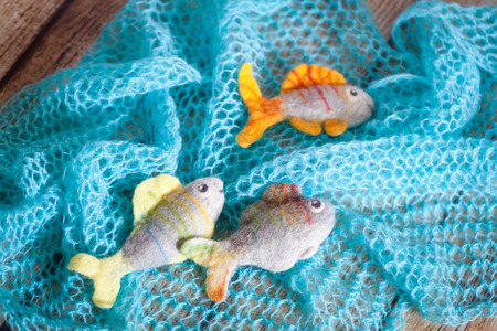 Beautiful colored felted fish on blue knitted shawl and wooden backgroundの写真素材