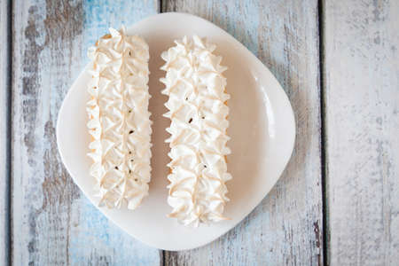 Eclairs with meringue frosting on a white plate on light wooden backgroundの写真素材