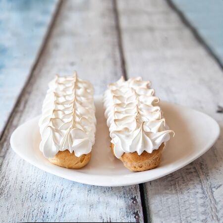 Eclairs with meringue frosting on light wooden background