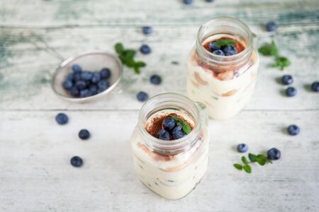 Homemade creamy tiramisu in glass jars with fresh blueberries, mint and cocoa for breakfastの写真素材