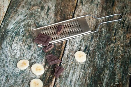 Banana and chocolate and metal grater for chocolate on wooden backgroundの写真素材
