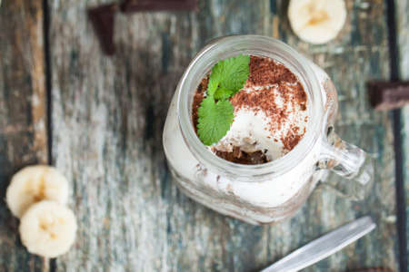 Healthy breakfast in glass mason jars. Served on wooden table with banana and chocolate over backgroundの写真素材