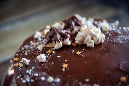 Christmas cake with chocolate glaze, star sprinkles and meringues on wood background. Close-upの写真素材