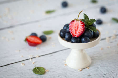 Strawberries and blueberries, fresh mint on white stand on light wood backgroundの写真素材