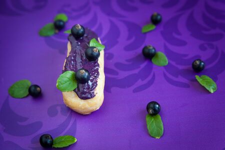 Eclair with cream and black currants on violet backgroundの写真素材