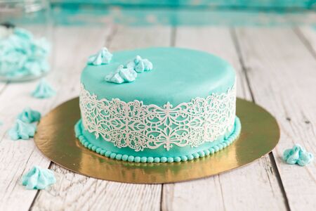 Elegant wedding cake with turquoise mastic and white lace icing decorated with meringues/kisses on wood backgroundの写真素材