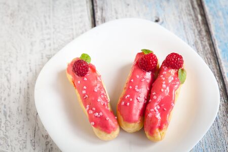 Eclair with cream and raspberry on a white plate on wood background