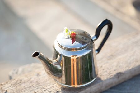 Teapot with strawberry and flowers outdoors