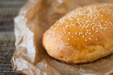 Loaf of rustic bread on a wrinkled baking paper and wooden background