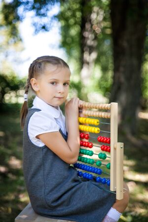Little school girl in a uniform with abacus. Back to school outdoors