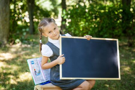 Little school girl in a uniform with a chalkboard. Back to school outdoors. Place for text