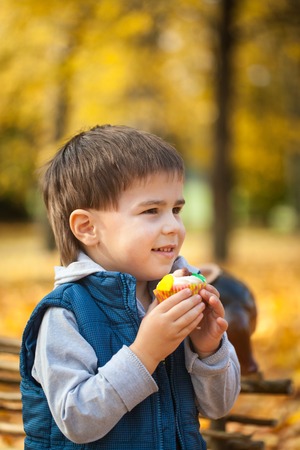 Young boy eating sweet cupcake in autumn park, vibrant autumn backgroundの写真素材