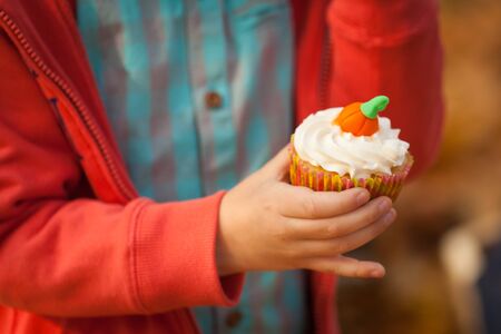 Sweet cupcake in a boy's hand, vibrant autumn backgroundの写真素材