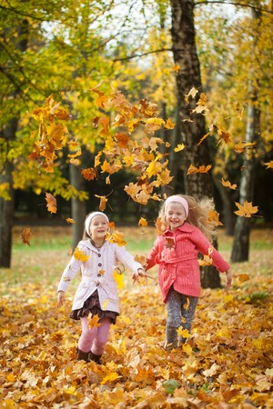 Two girls throwing leaves in autumn park, vibrant autumn backgroundの写真素材