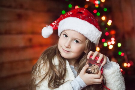 Girl in a christmas hat with a present in front of decorated treeの写真素材