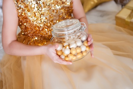 Gold candies in a glass jar in girls hands. Christmas timeの写真素材