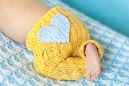 Newborn baby girl in a yellow hat and panties with blue heart sleeping on a soft white and blue knit blanketの写真素材