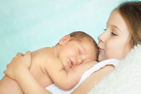 Cute little girl kissing her sleeping newborn sister in a pink lace panties and knit headbandの写真素材