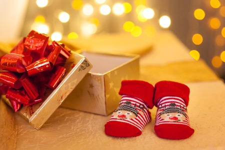 Baby red socks and christmas presents in front of a new year gold lights.の写真素材