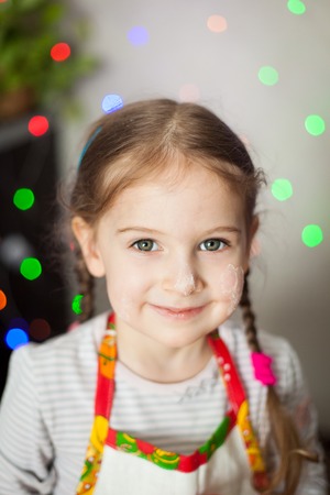 Happy little girl portrait, face smeared with flour. Christmas lights on backgroundの写真素材