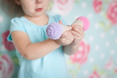 Little girl hands with a knitted ice-cream toys.