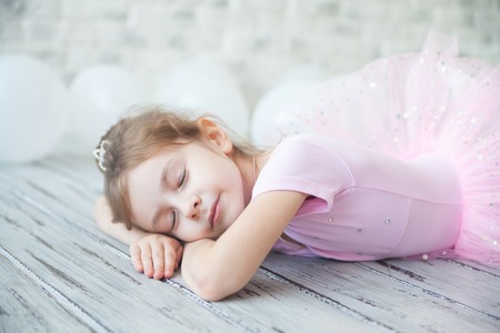 Little ballerina laying on a light wood floor with white balloons.の写真素材