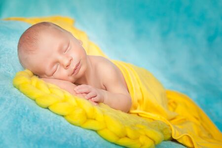 Sleeping cute newborn baby on a yellow chunky knit blanketの写真素材