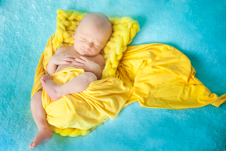 Sleeping cute newborn baby on a yellow chunky knit blanketの写真素材
