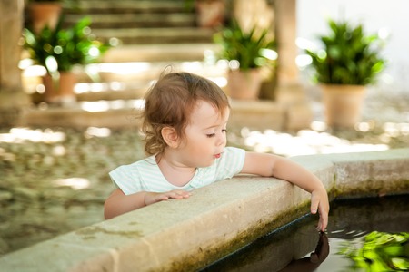 Small girl wets hands in a fountain in Alfabia gardens in Mallorca, Spainの写真素材