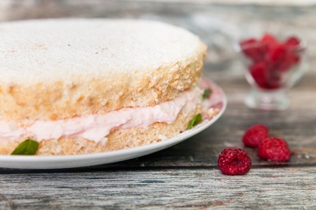 Fresh biscuit cake with raspberry yoghurt cream sprinkled with powdered sugar and fresh raspberries on wooden backgroundの写真素材