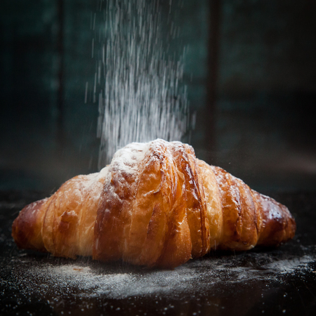 Tasty croissant for breakfast sprinkled with powdered sugar on dark backgroundの写真素材