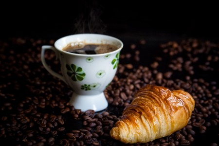 Tasty croissants for breakfast with a cup of coffee on bean backgroundの写真素材