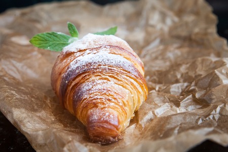 Tasty croissants with powdered sugar on a crumpled paper on dark background