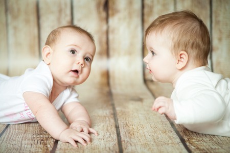 Two cute 6 months girls lie on thier stomach on wooden backgroundの写真素材